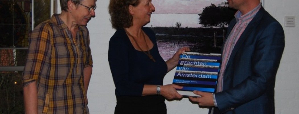 Gertjan van der Hoeven overhandigt het boek “De grachten van Amsterdam” aan Christine Kempkes en Corrie de Boer van de bibliotheek